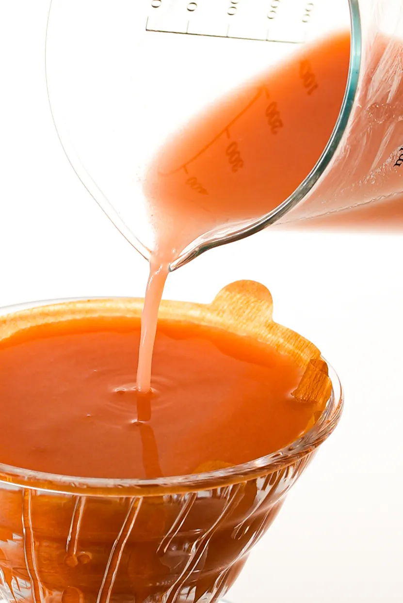 A pink-orange mixture poured from a beaker into a glass