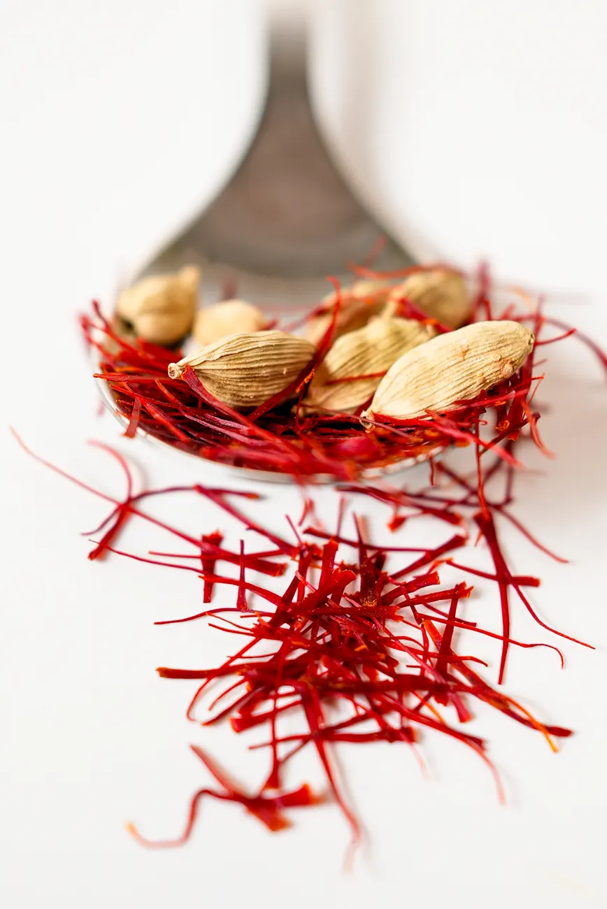 Cardamom pods resting on saffron threads on a spoon